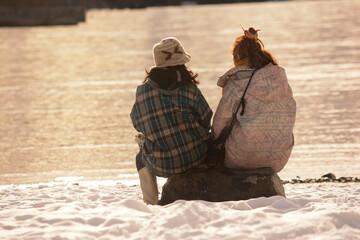 two ladies sitting in the snow by a lake