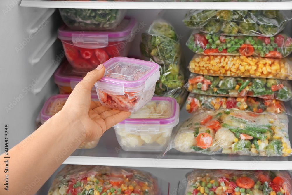 Woman putting container with frozen vegetables into refrigerator