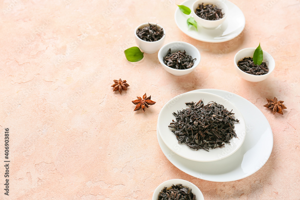 Bowls with dry black tea leaves on color background