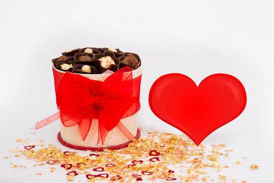 Valentine's Day. White box with a red bow with sweets on a white background with a big heart with gold powder with hearts