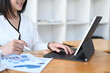 © Prathankarnpap - Businesswoman working on tablet computer and analyzing marketing research charts on paper document at office.