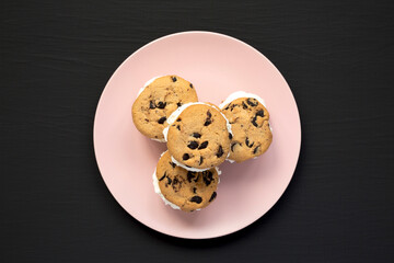 Homemade Chocolate Chip Cookie Ice Cream Sandwich on a pink plate on a black surface, top view. Overhead, from above, flat lay.