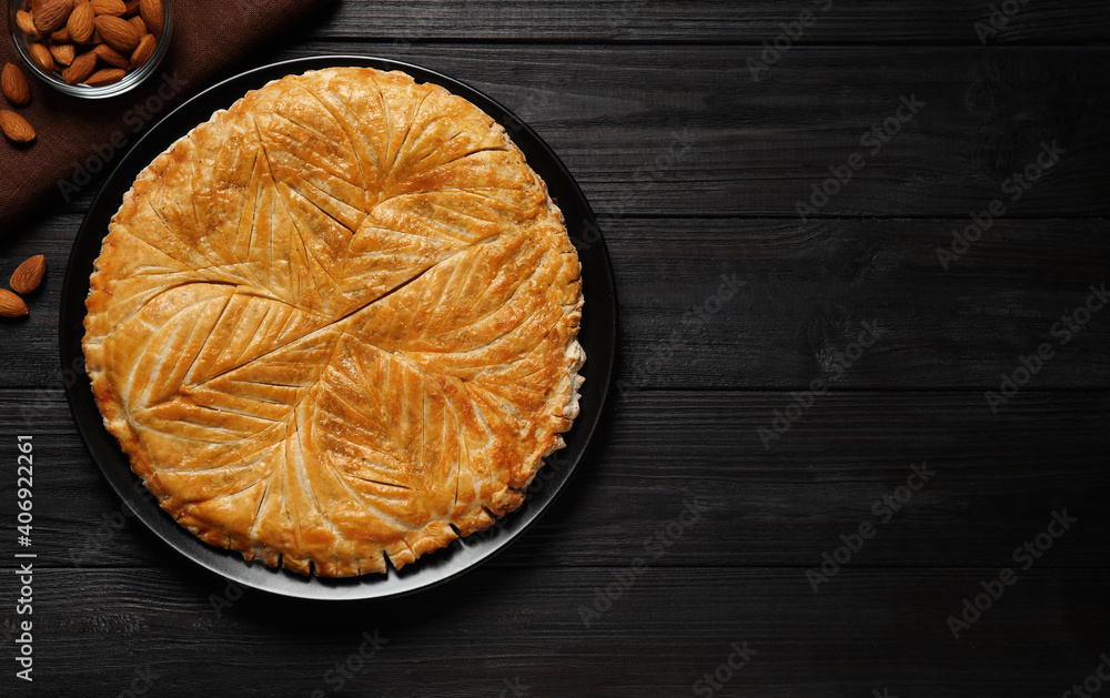 Traditional galette des rois and almonds on black wooden table, flat lay. Space for text - obrazy, fototapety, plakaty 