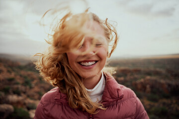 portrait of young smiling woman face partially covered with flying hair in windy day standing at mou