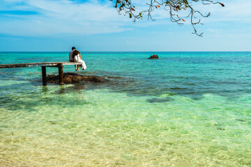 Wall Mural - happy young couple sitting on wood bridge and sea beach at Koh MunNork Island, Rayong, Thailand