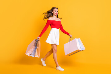 Poster - Full length body size photo girl smiling looking blank space stepping with packages from store isolated on bright yellow color background