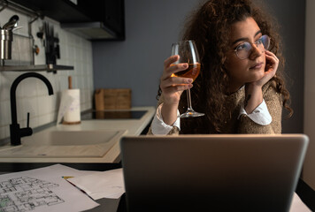 Portrait of young woman working at home in kitchen using laptop.