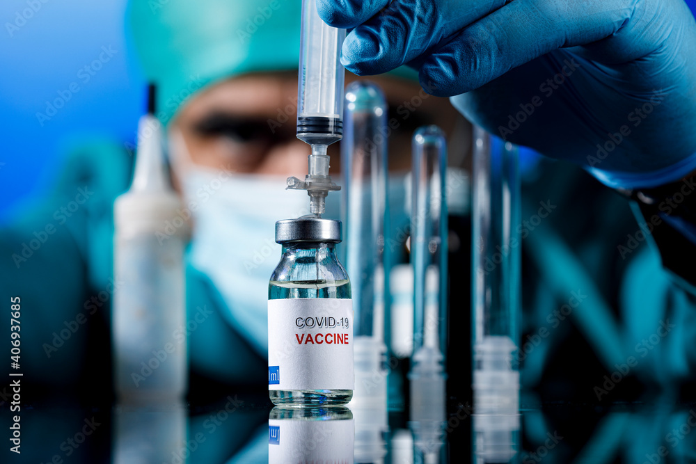 Medico con protezioni mediche e guanti in lattice preleva del il  vaccino anti-covid con una siringa  in un tavolo con diverse fialette  - obrazy, fototapety, plakaty 