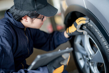 Wall Mural - Asian auto mechanic holding digital tablet checking car wheel and tire in auto service garage. Mechanical maintenance engineer working in automotive industry. Automobile servicing and repair concept