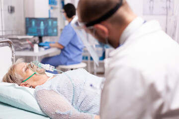 doctor checking senior woman with oxygen mask breathing hard because of infection with covid19. pati