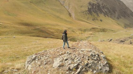 Wall Mural - Attractive caucasian female backpacker stands on rock in scenic location and enjoys dramatic mountains