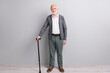 © deagreez - Full size photo of optimistic old man stand with stick wear dark sweater trousers isolated on grey wall
