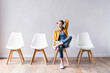 © LIGHTFIELD STUDIOS - Young woman using headphones while waiting on chair in hall
