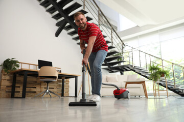 Canvas Print - Young man using vacuum cleaner in living room