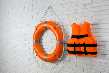 Orange life jacket and lifebuoy on white brick wall. Rescue equipment