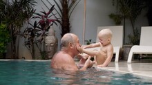 Special Bond Between Grandfather And His Grandchild. Grandpa Kisses And Plays With Adorable Caucasian Toddler In The Private Swimming Pool