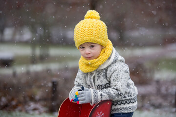 Sticker - Beautiful blond toddler child, boy, with handmade knitted sweater playing in the park with first snow