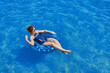 © Konstantin Savusia - Young red-haired woman floats on the ocean in swimming circle. Girl with glasses resting on sea on inflatable ring. Black fashionable swimsuit. Summer holidays at sea. Cheerful person on vacation.