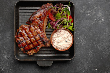 Wall Mural - Grilled chalagach with sauce, vegetables and herbs, on a black pan, on a dark background