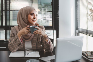 Wall Mural - Confident asian muslim business woman brown hijab sitting and working with laptop computer at modern office.