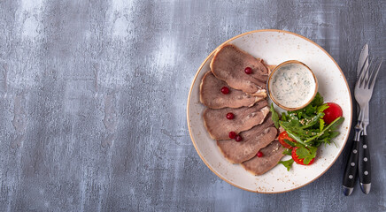 Wall Mural - Sliced beef tongue on a plate served with fork and knife. Top view, text space