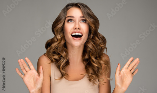 Beautiful shocked and surprised woman screaming and  looking up presenting  your product . Curly hair girl amazed . Expressive facial expressions . Beauty and cosmetology