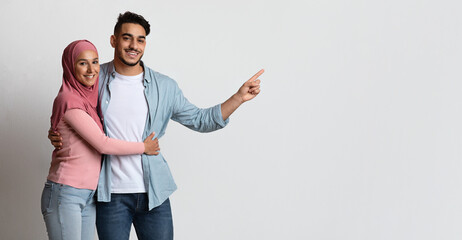 Wall Mural - Happy Muslim Couple Embracing And Pointing Aside At Copy Space