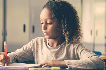 Positive female school teacher helping curly haired girl to do her task. Schoolgirl drawing in her copybook in class. Education or back to school concept