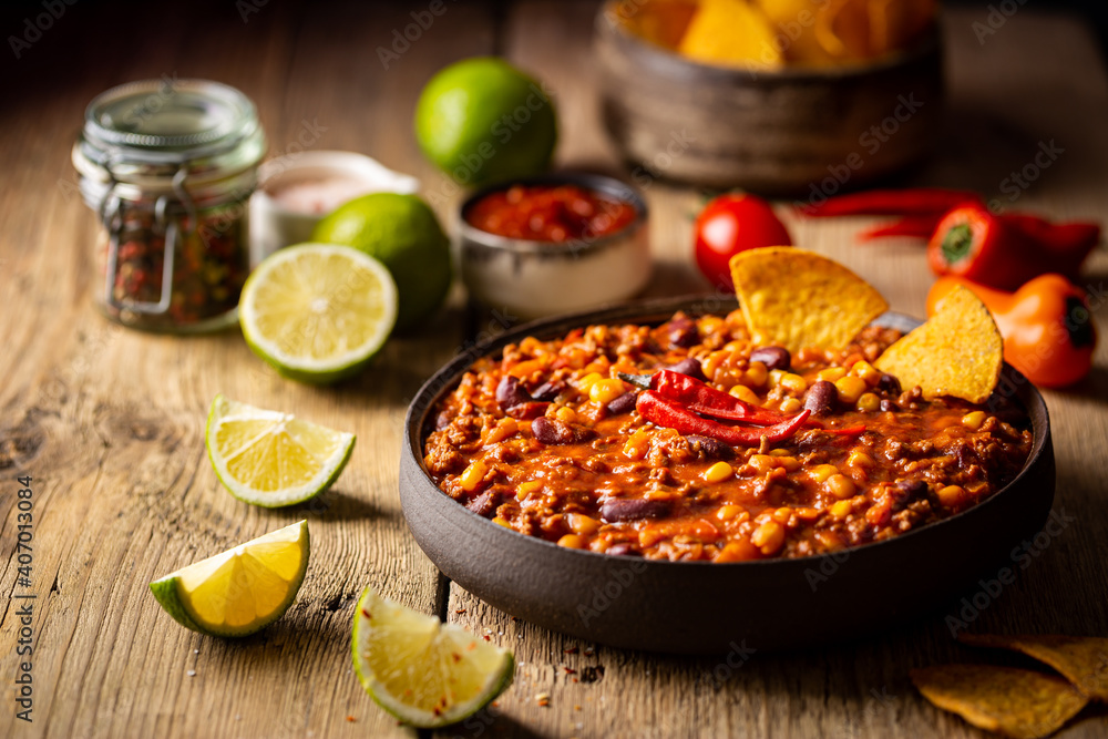 Mexican hot chili con carne in a bowl with tortilla chips on wooden background - obrazy, fototapety, plakaty 