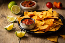 Single Big Black Plate Of Yellow Corn Tortilla Nachos Chips With Salsa Sauce Over Wooden Table