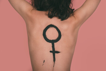 Caucasian woman with the female symbol painted on her back with pink background. Feminism concept