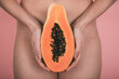 woman's hands holding a papaya in front of the hips with pink background. concept femininity. concept empowerment