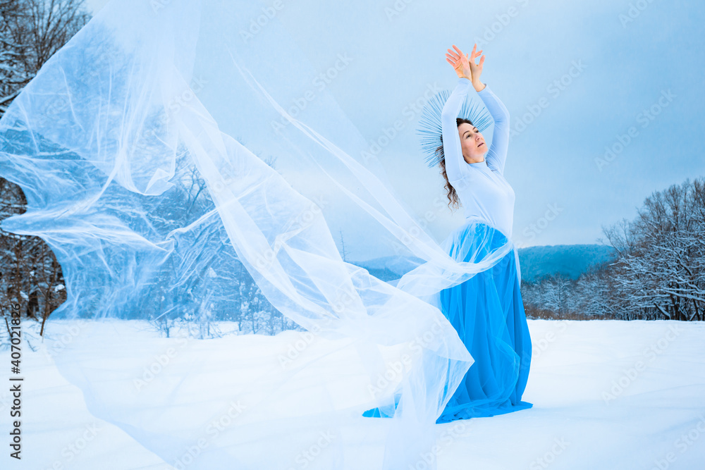 A fairy-tale woman in a blue dress with a fluttering train in the image of a snow queen in a winter forest. Stock Photo | Adobe Stock A fairy-tale woman in a blue dress with a fluttering train in the image of a snow queen in a winter forest. Stock Photo | Adobe Stock