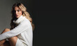 © EkaterinaJurkova - Young beautiful long-haired woman in a white knitted sweater in the studio on a black background. The woman is sitting and posing for the photographer.