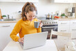 Mobile Office at home. Young woman sitting in kitchen at home working using on laptop computer. Lifestyle girl studying or working indoors. Freelance business quarantine concept.