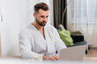 © LIGHTFIELD STUDIOS - Bearded man in bathrobe using laptop near cup on blurred foreground in hotel room