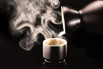 Sake, pouring traditional distilled and fermented alcohol from Japan, served hot. Black background with space for text