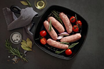 Raw meat sausages with herbs, spices and vegetables on dark concrete background. Flat layot, copy space