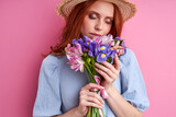 Fototapeta Tulipany - woman inhales the scent of flowers, tender redhead female with boquette of summer flowers isolated on pink