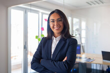Confident Latin Business Leader Portrait. Young Businesswoman In Suit And Glasses Posing With Arms Folded, Looking At Camera And Smiling. Female Leadership Concept