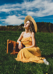 Sticker - girl in yellow dress and suitcase sitting on mountain meadow with dandelions