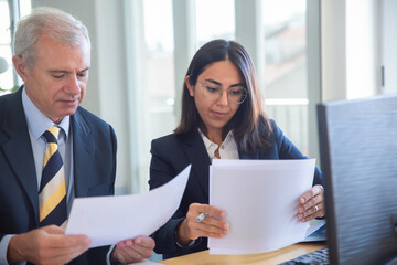 Wall Mural - Focused diverse business people reading document at workplace. Male client consulting female expert. Teamwork or cooperation concept