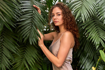 Wall Mural - woman in beige elegant silk dress posing in tropical garden. natural beauty, perfect face, bronze skin