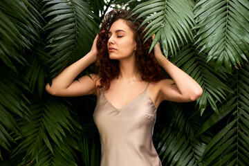 Wall Mural - woman in beige elegant silk dress posing in tropical garden. natural beauty, perfect face, bronze skin