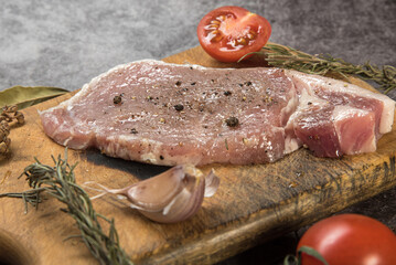 Fresh meat, pork carbonate on a cutting board with tomatoes and spices on a gray mottled background