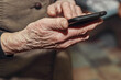 © olgasalt - Old woman's wrinkled hands hold a modern mobile phone