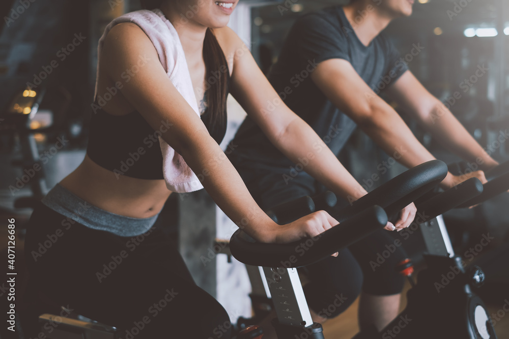 Asian man and woman they are enjoys cycling in the gym because it keeps his legs strong and healthy. - obrazy, fototapety, plakaty 