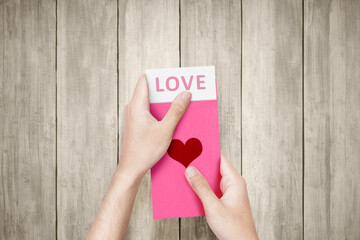 human hand opening a pink envelope with heart shape with love text on the paper