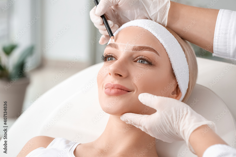 Young woman undergoing eyebrow correction procedure in beauty salon