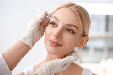 Young woman undergoing eyebrow correction procedure in beauty salon